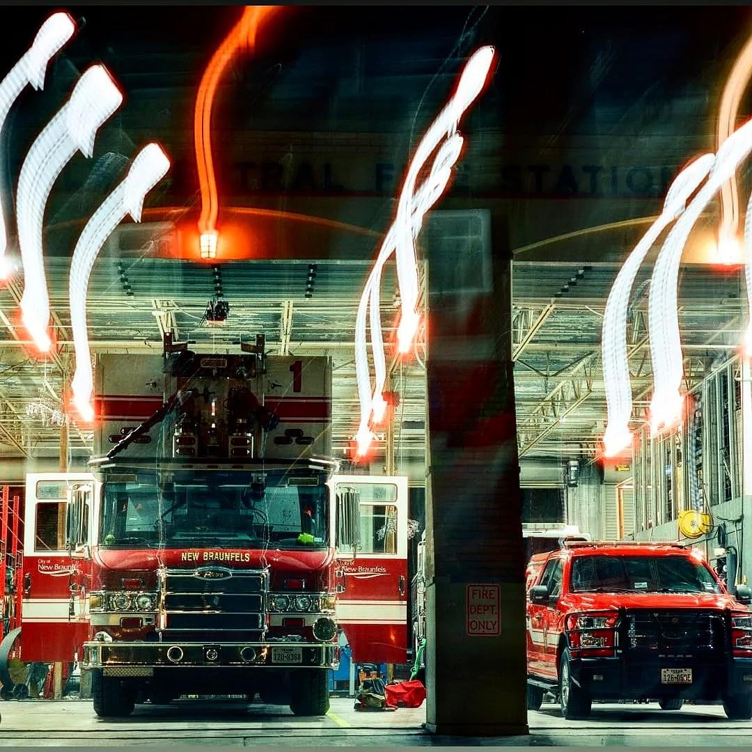 A fire truck and a red pickup truck are parked inside a fire station with light trails overhead.