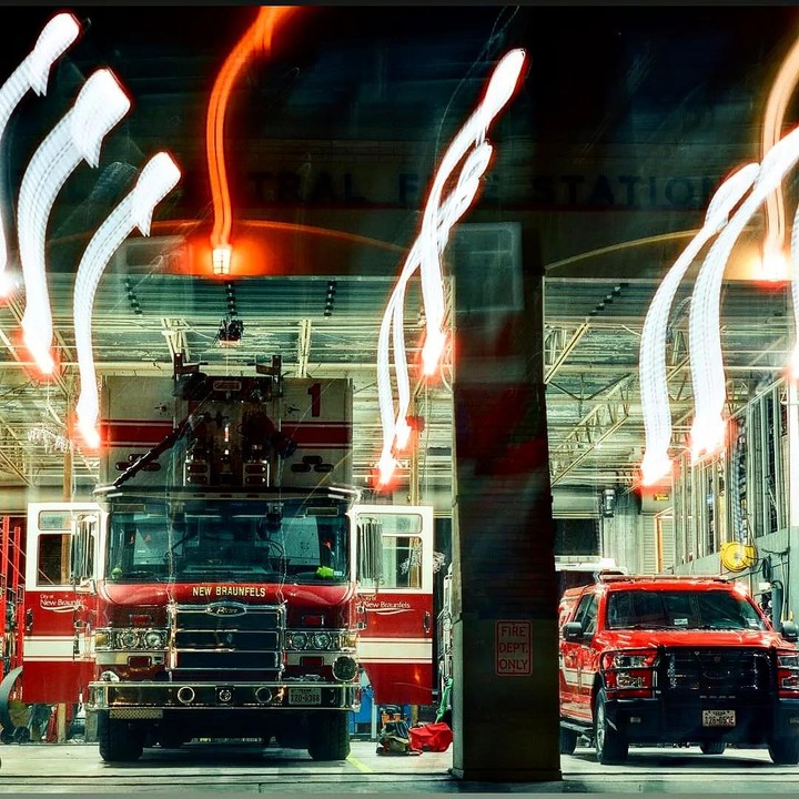 A fire truck and a red pickup truck are parked inside a fire station with light trails overhead.