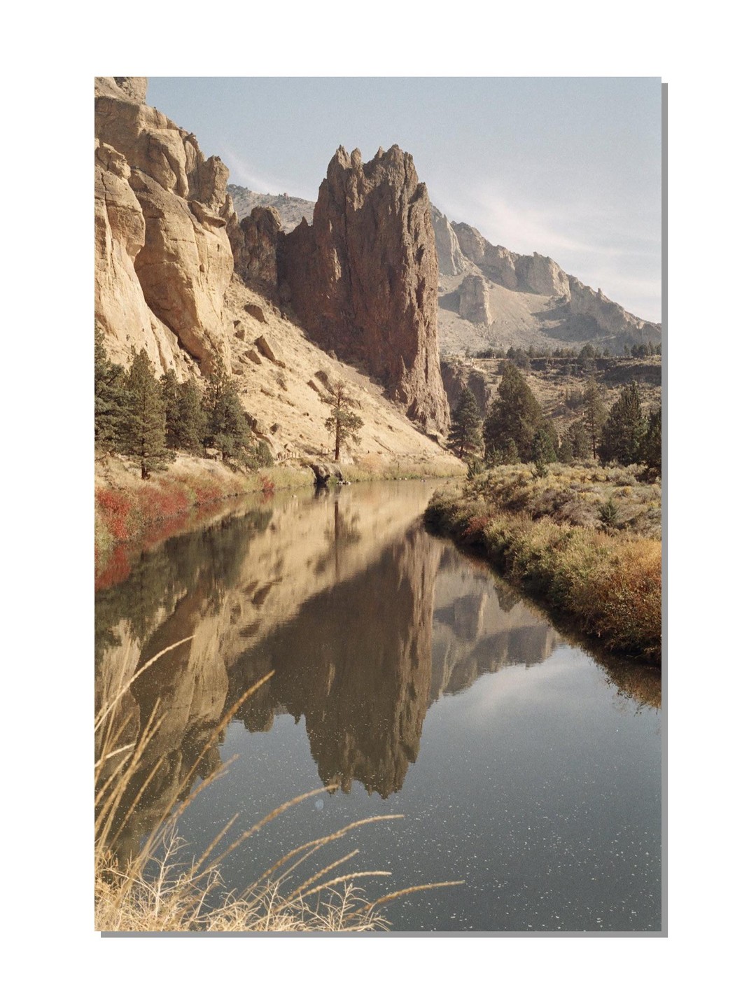 A river reflects towering rock formations and a clear sky under a bright sun.