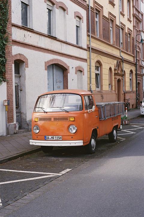 An orange pickup truck is parked on a street next to a building with brick accents.