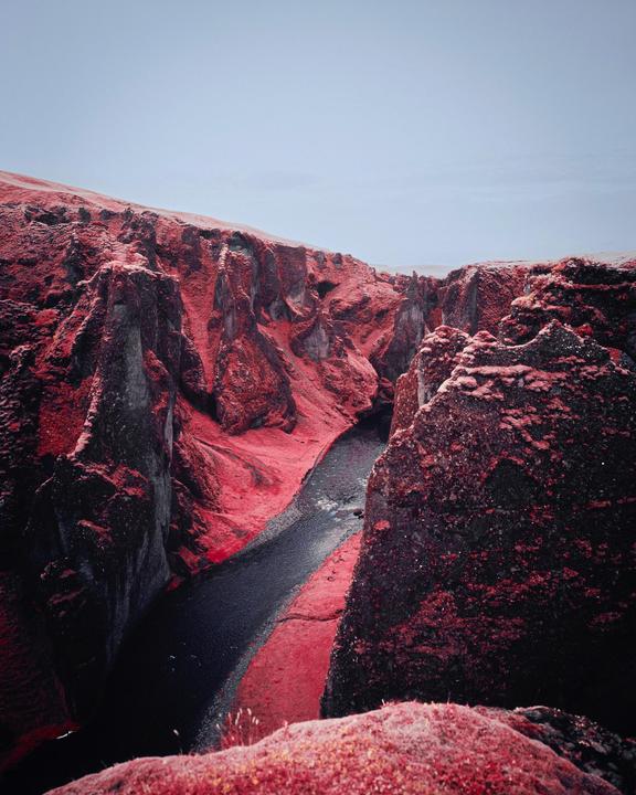 A river flows through a canyon with red foliage on its banks and cliffs.