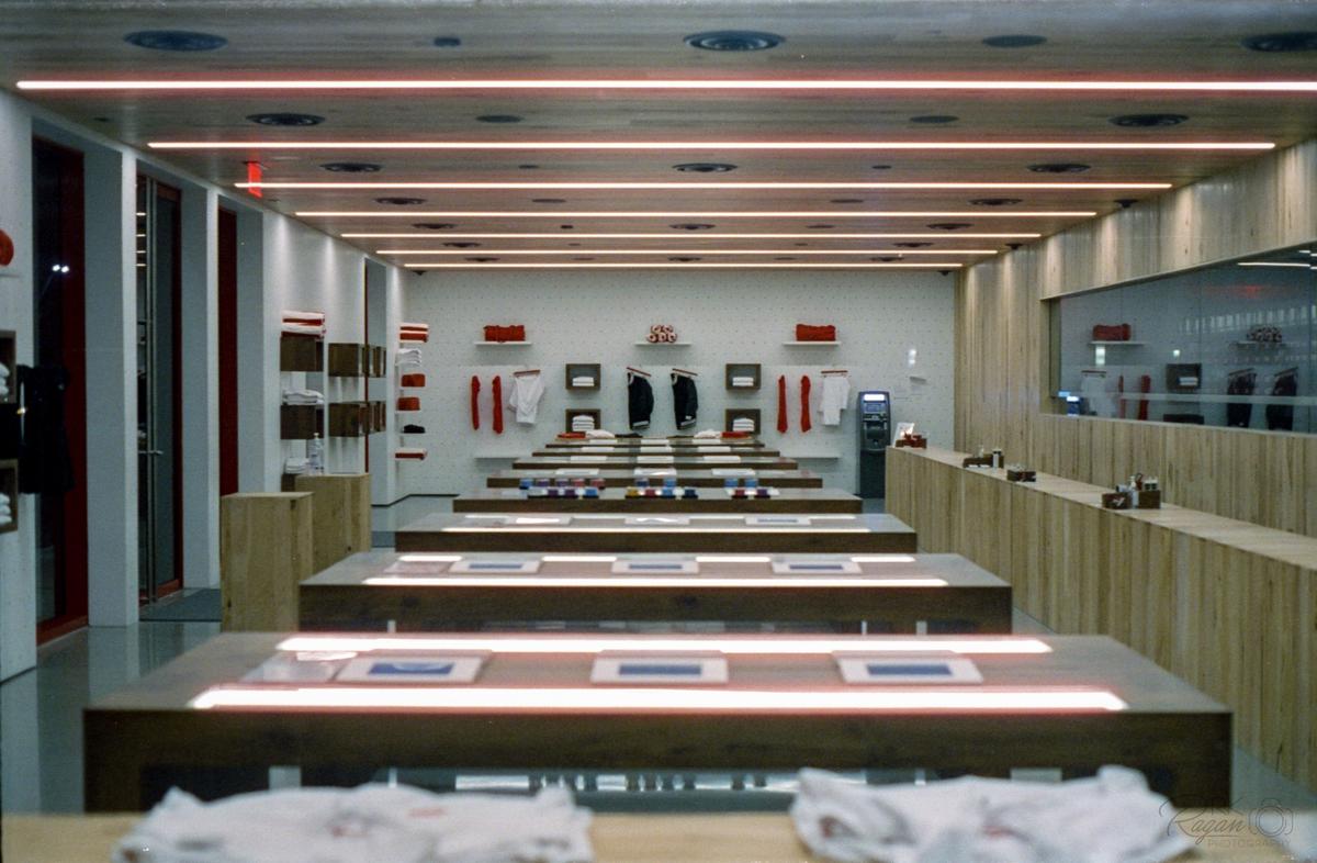 A clothing store interior features multiple display tables with illuminated strips and shelves of folded garments.
