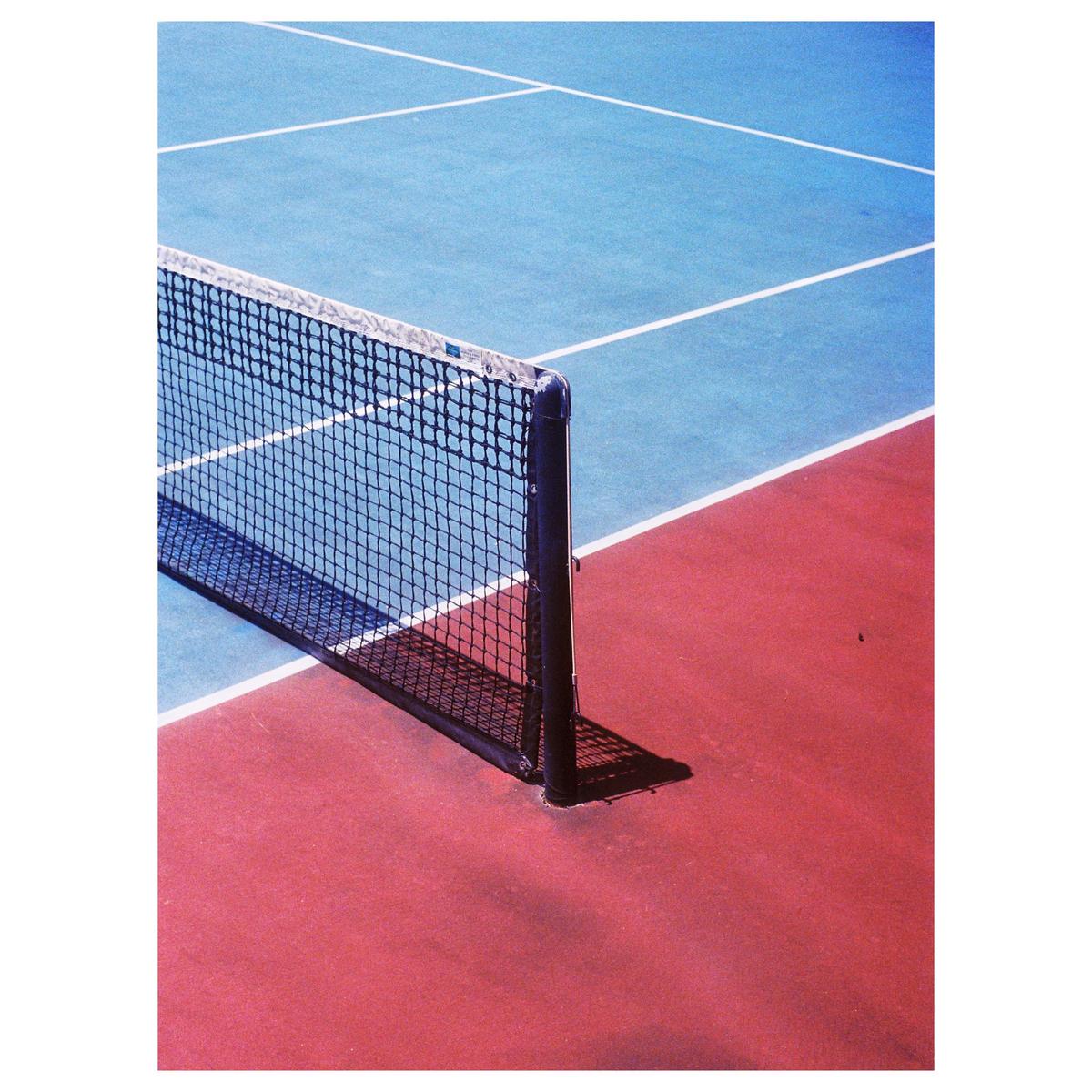 A tennis court net casts a shadow on the red and blue court.