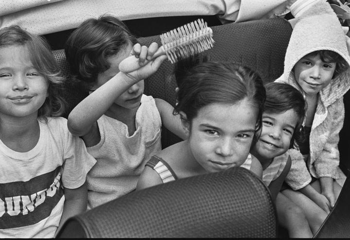 Five children are sitting in a car, one of whom is brushing another child's hair.