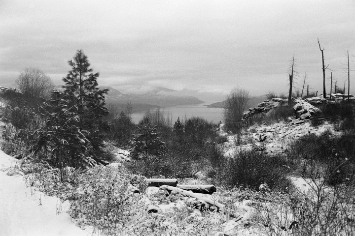 A snowy landscape with a lake and mountains in the distance is seen from a high vantage point.