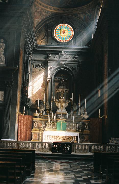 Sunlight streams through a stained glass window and illuminates the altar of a church.