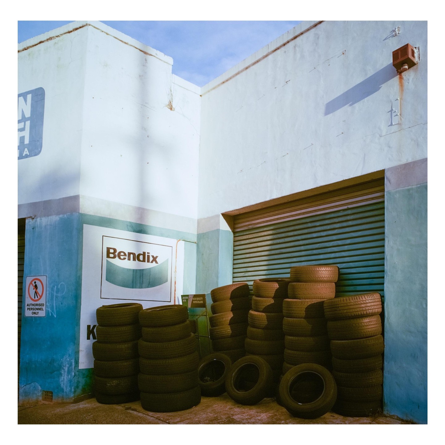 Numerous stacks of tires are piled against the light blue and white walls of a building with a closed garage door.