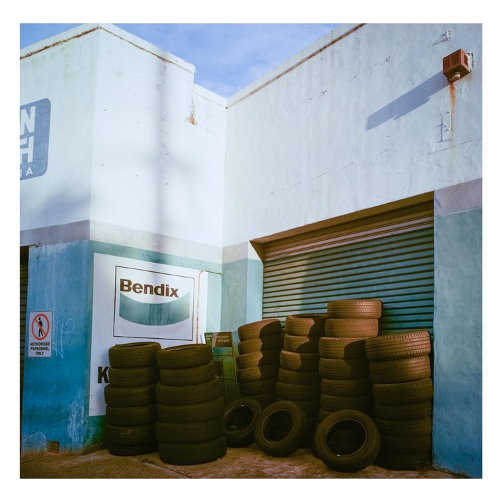 Numerous stacks of tires are piled against the light blue and white walls of a building with a closed garage door.