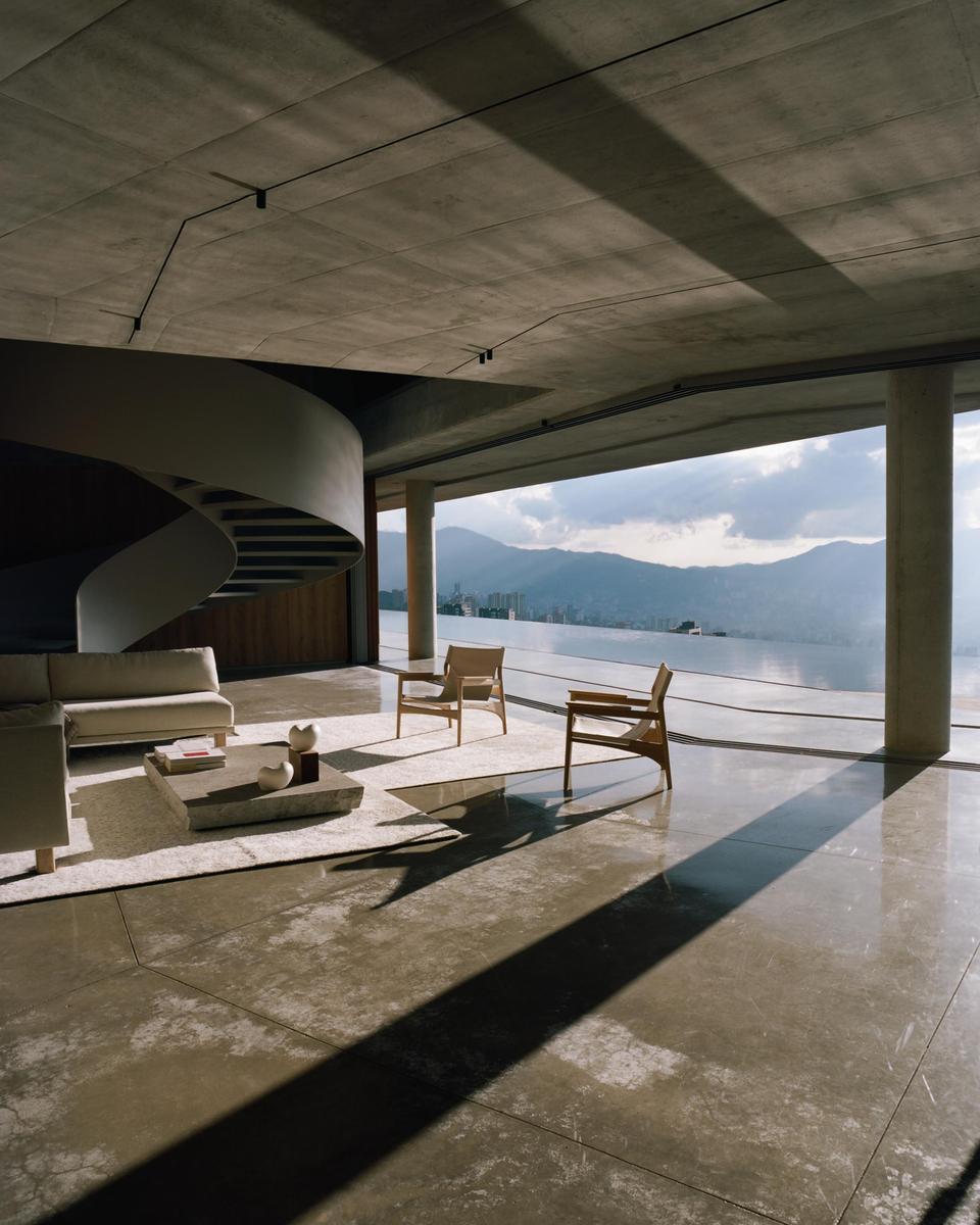 A modern living room with a spiral staircase and concrete floor overlooks a lake and mountains.