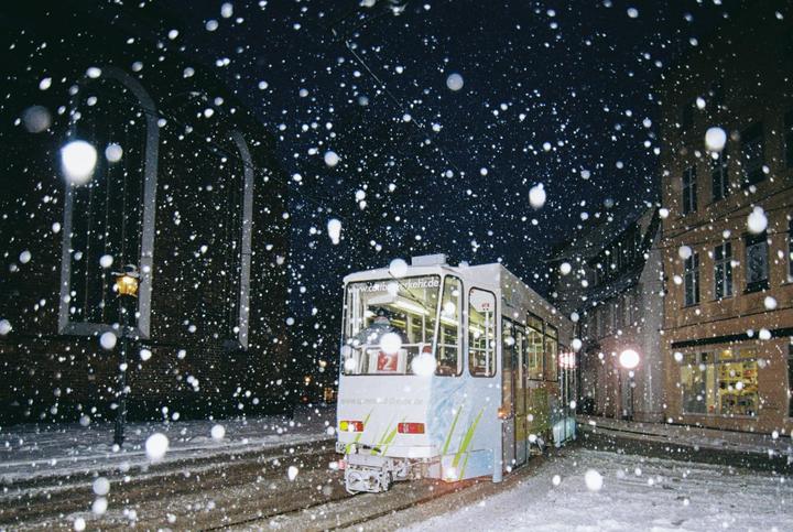 A tram is visible on a snowy street at night, with large snowflakes falling.