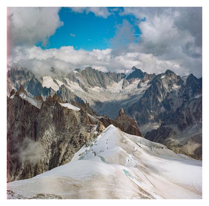 A vast mountain range with snow-capped peaks and glaciers is visible under a partly cloudy sky.