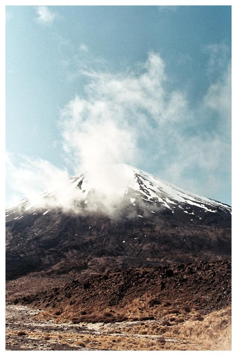 A snow-capped mountain peak is partially obscured by clouds under a blue sky.