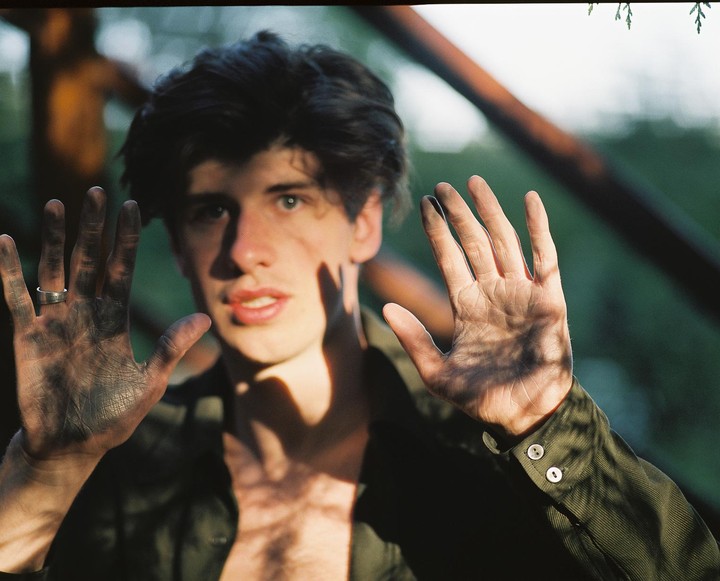 A man with dirty hands presses them against a transparent surface, looking directly at the viewer.
