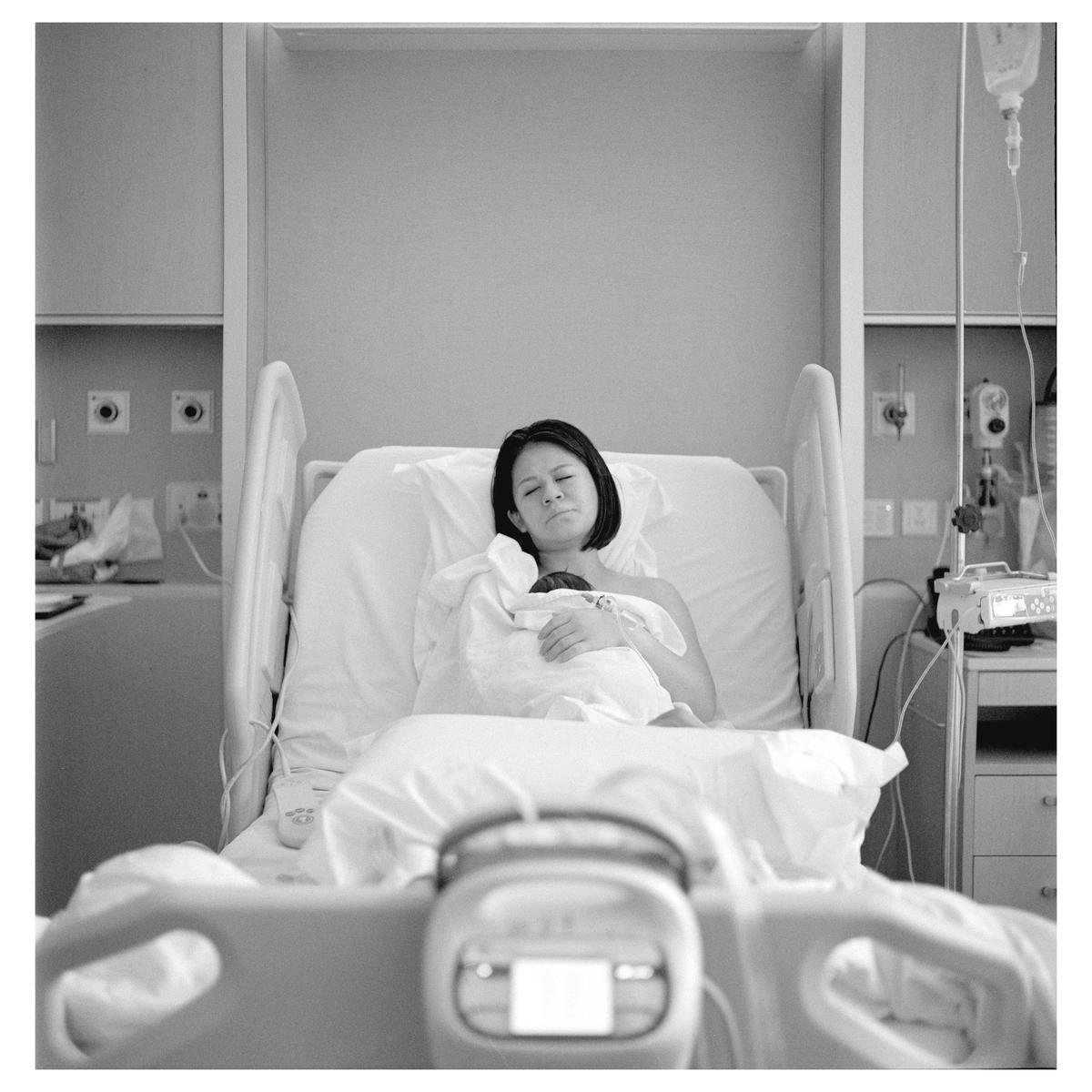 A woman lies in a hospital bed holding a newborn baby.