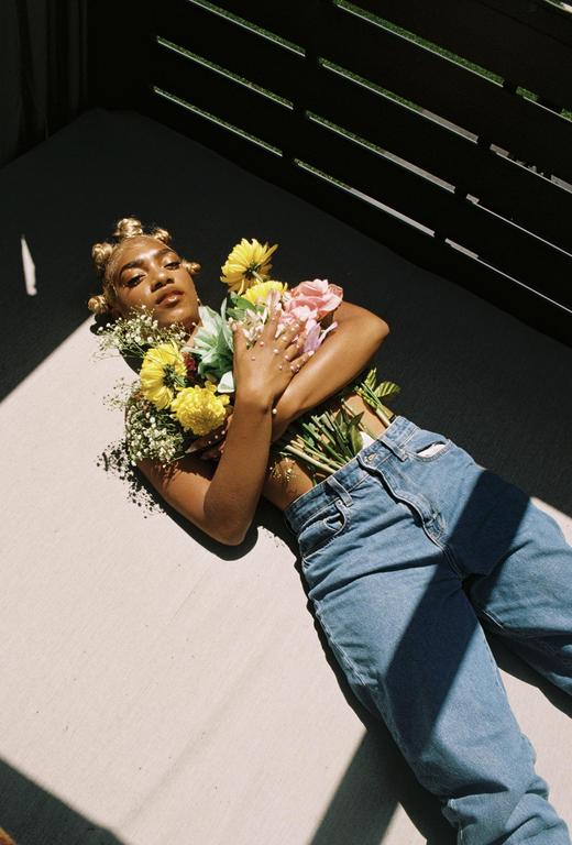 A woman lies on the ground with flowers on her chest and in her jeans.
