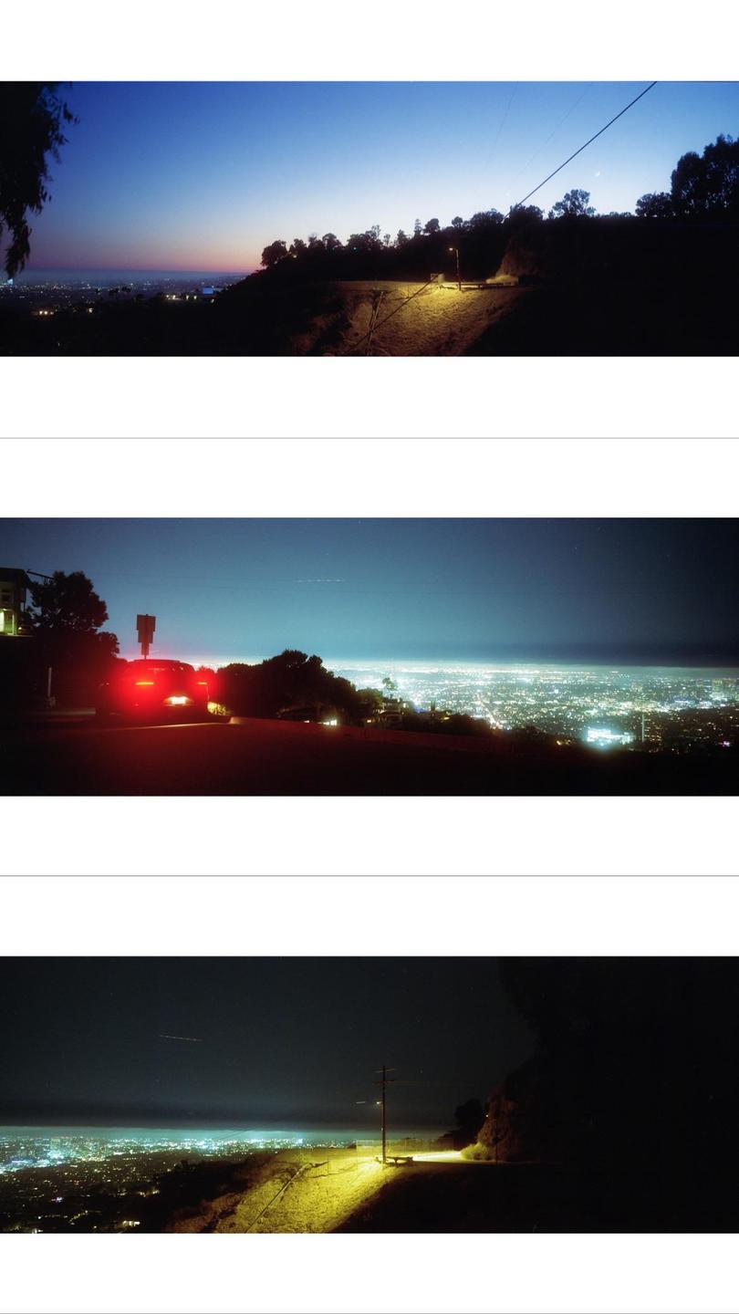 A panoramic view of a city at night, seen from a hill with a street light illuminating the foreground.
