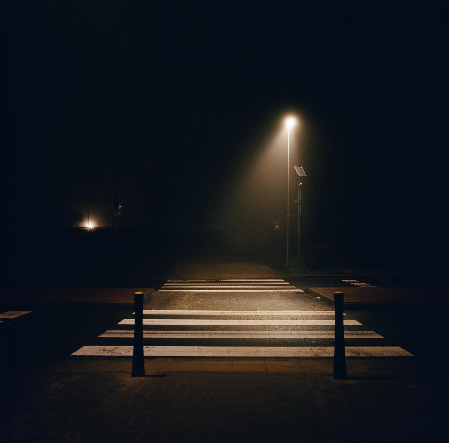 A street light illuminates a crosswalk on a foggy night.