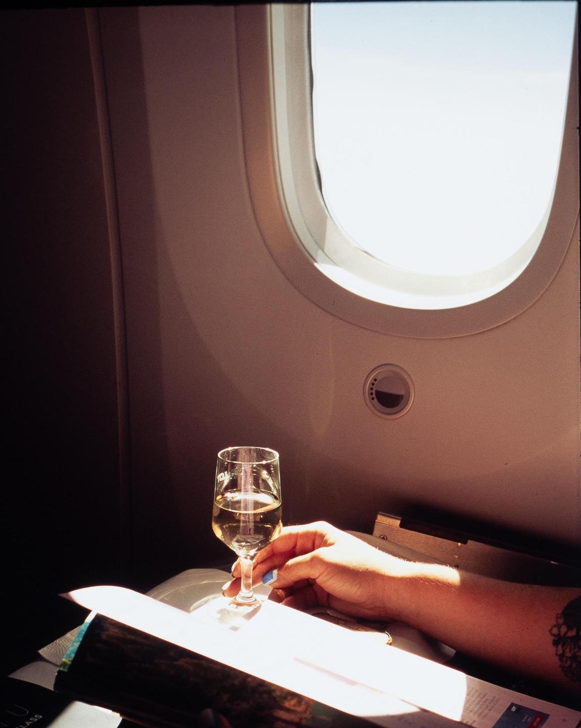 A hand holds a glass of champagne next to an airplane window.