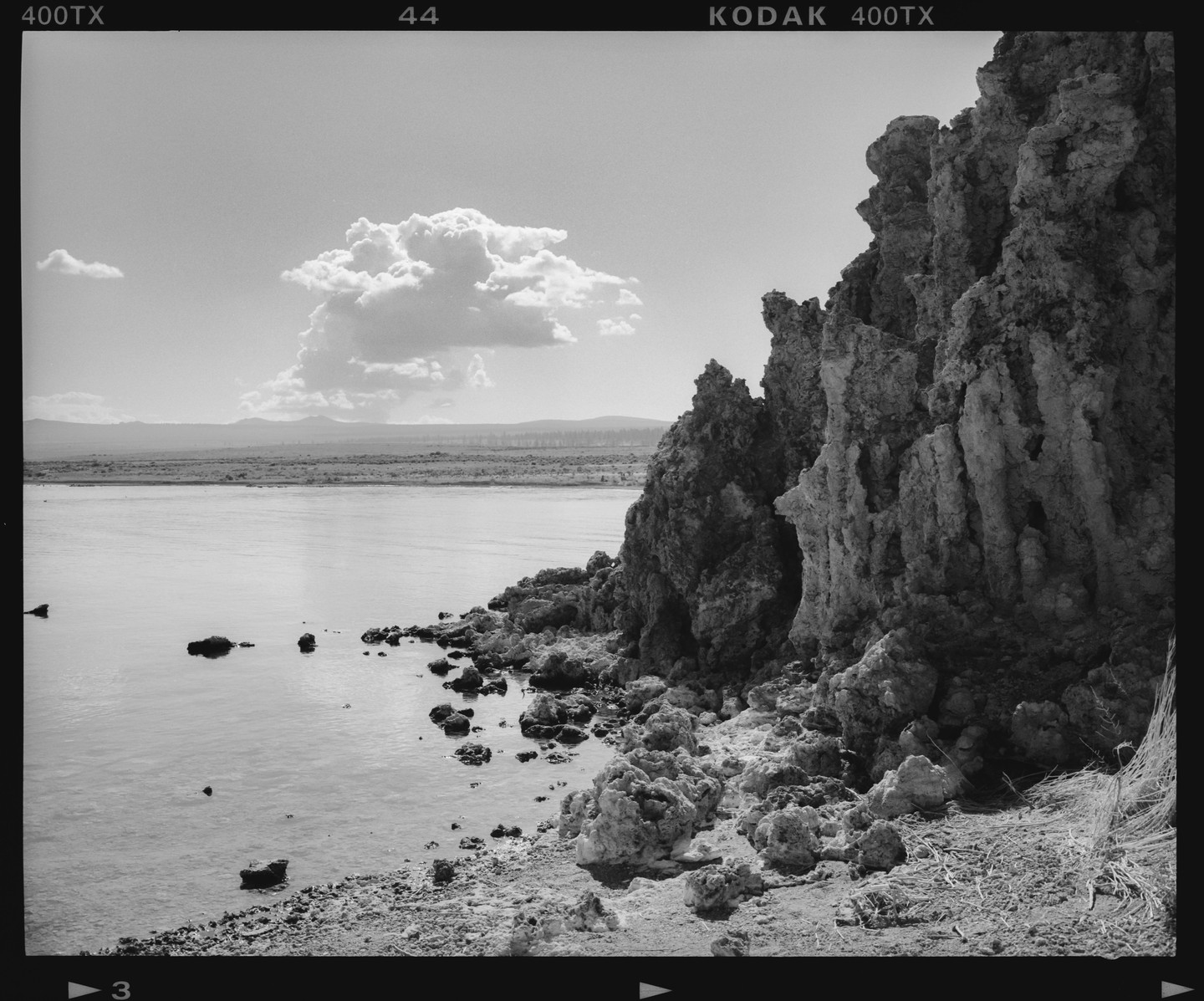A large cloud floats above a lake with tufa formations along its shore.