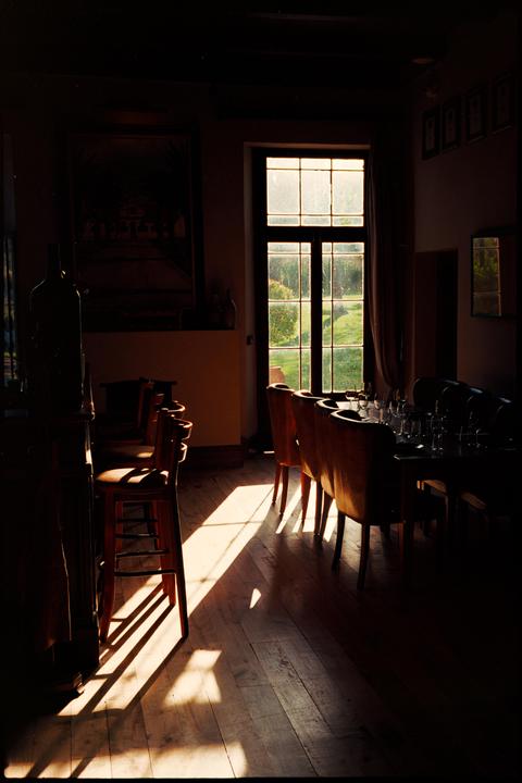 Sunlight streams through a tall window into a dining room with tables and chairs.