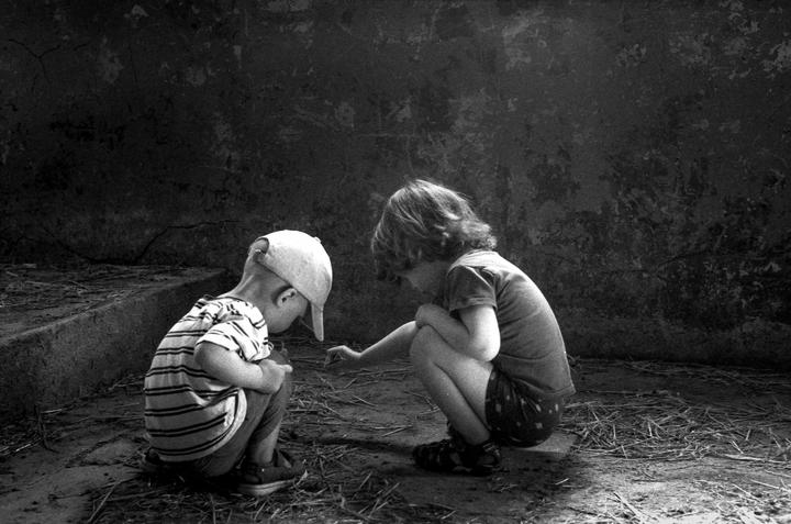 Two children crouch on the ground, looking at something in front of them.