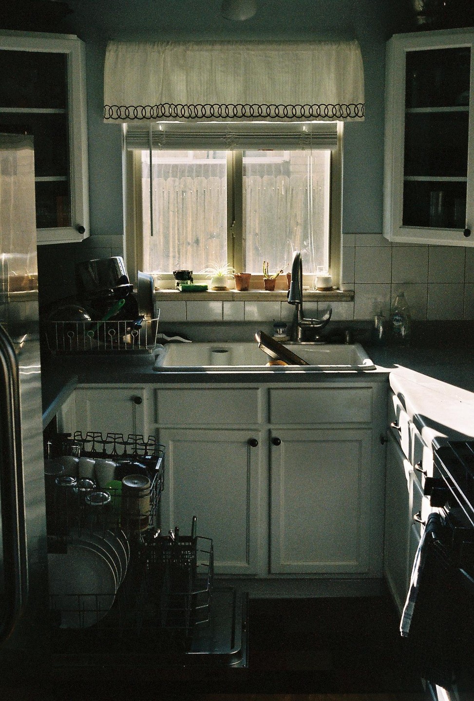 Sunlight streams through a kitchen window, illuminating a sink filled with dishes and a partially open dishwasher.