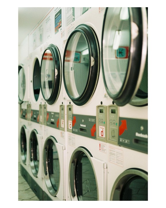 A row of washing machines and dryers with their doors open is visible in a laundromat.