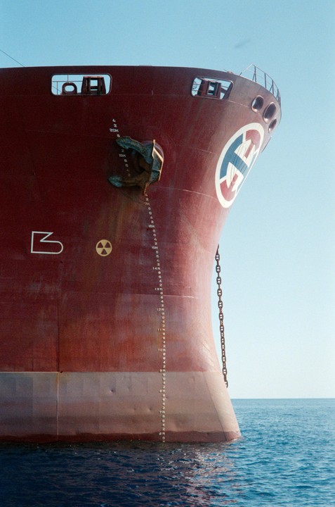 The bow of a large red ship with a white and blue logo is visible above the water.