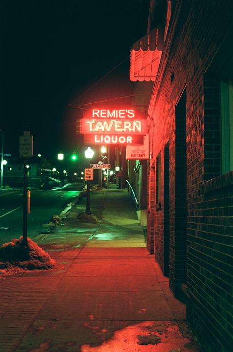 A neon sign for Remie's Tavern and Liquor illuminates a brick building and sidewalk at night.