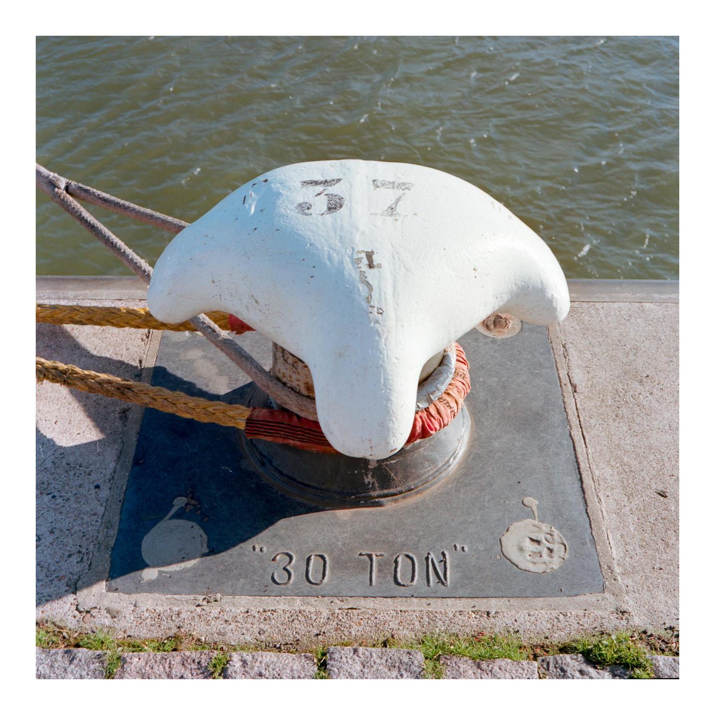 A white bollard with a rope wrapped around it sits on a dock next to water.