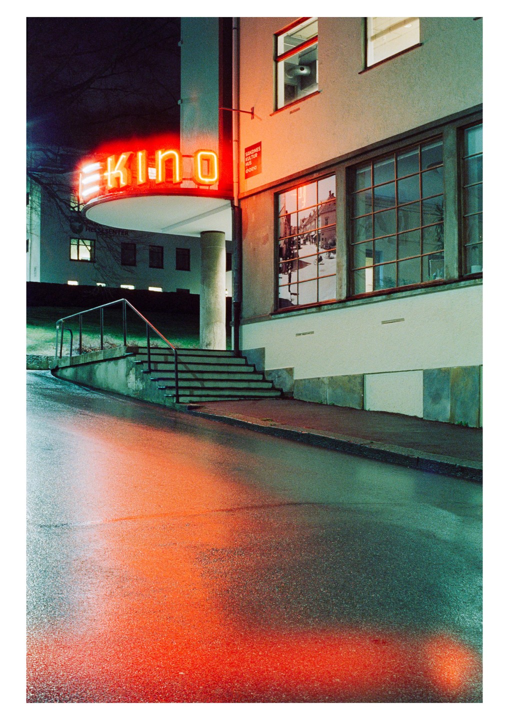 A neon sign for "KINO" illuminates a wet street and building at night.