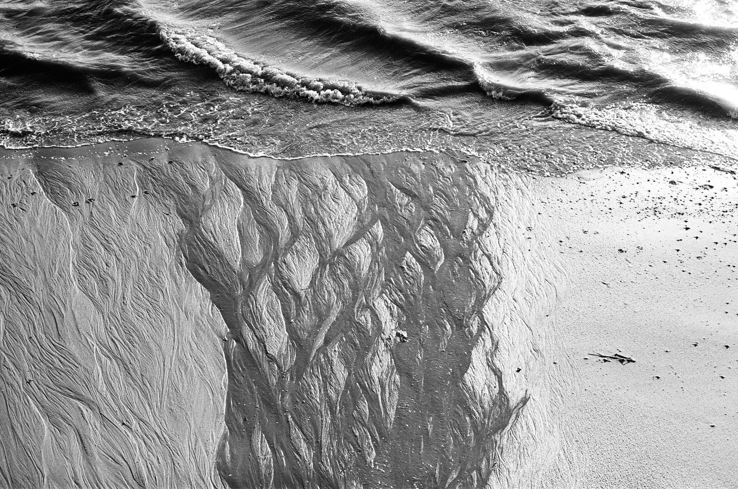 Waves wash over a sandy beach with intricate patterns carved into the sand.