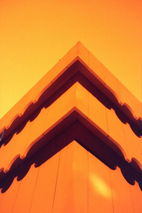A building with multiple levels and decorative edges is shown from a low angle against a bright sky.