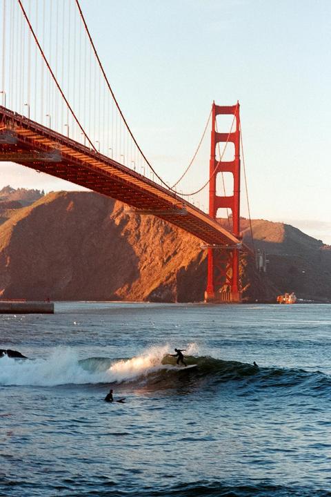 A surfer rides a wave in front of the Golden Gate Bridge.