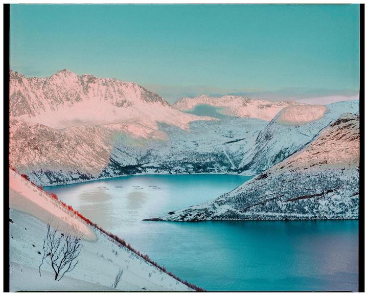A body of water is surrounded by snow-covered mountains under a clear sky.