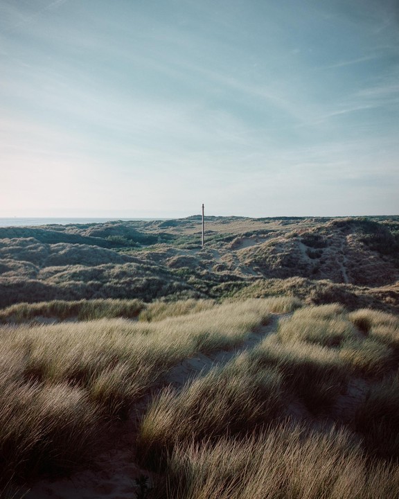A vast expanse of grassy dunes stretches towards the sea under a clear sky.