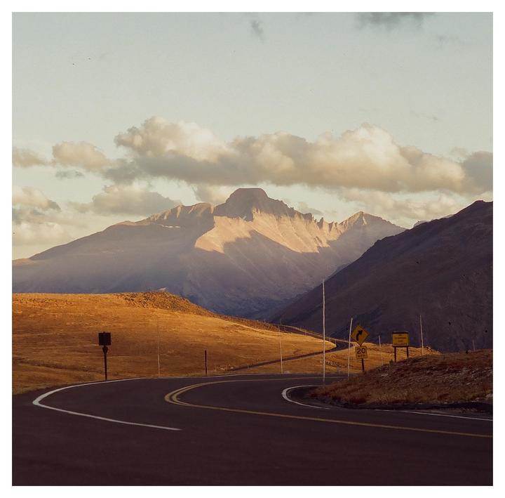 A winding road leads through a mountainous landscape under a cloudy sky.