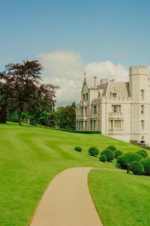 A path curves through a green lawn towards a large stone building with turrets.