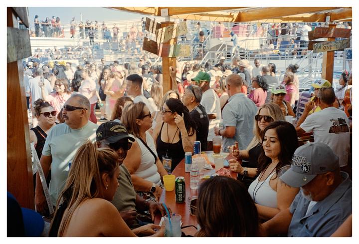 A large group of people are gathered at an outdoor bar on a sunny day.