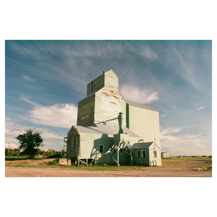 A large, light green grain elevator stands under a blue sky with scattered clouds.