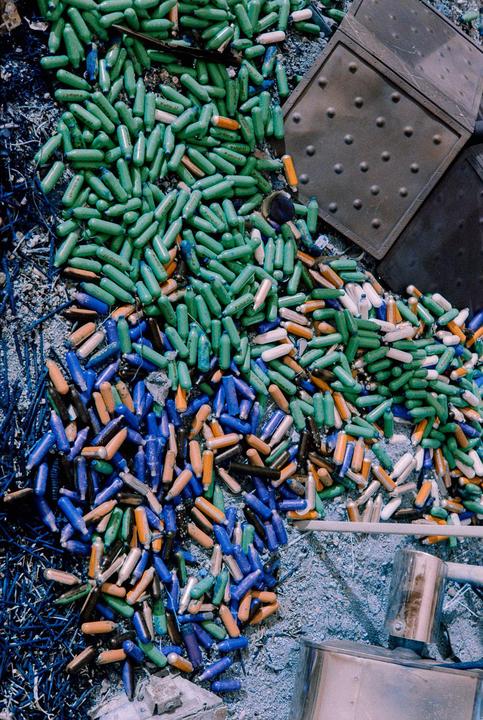 A pile of colorful gas canisters is scattered on the ground next to metal objects.