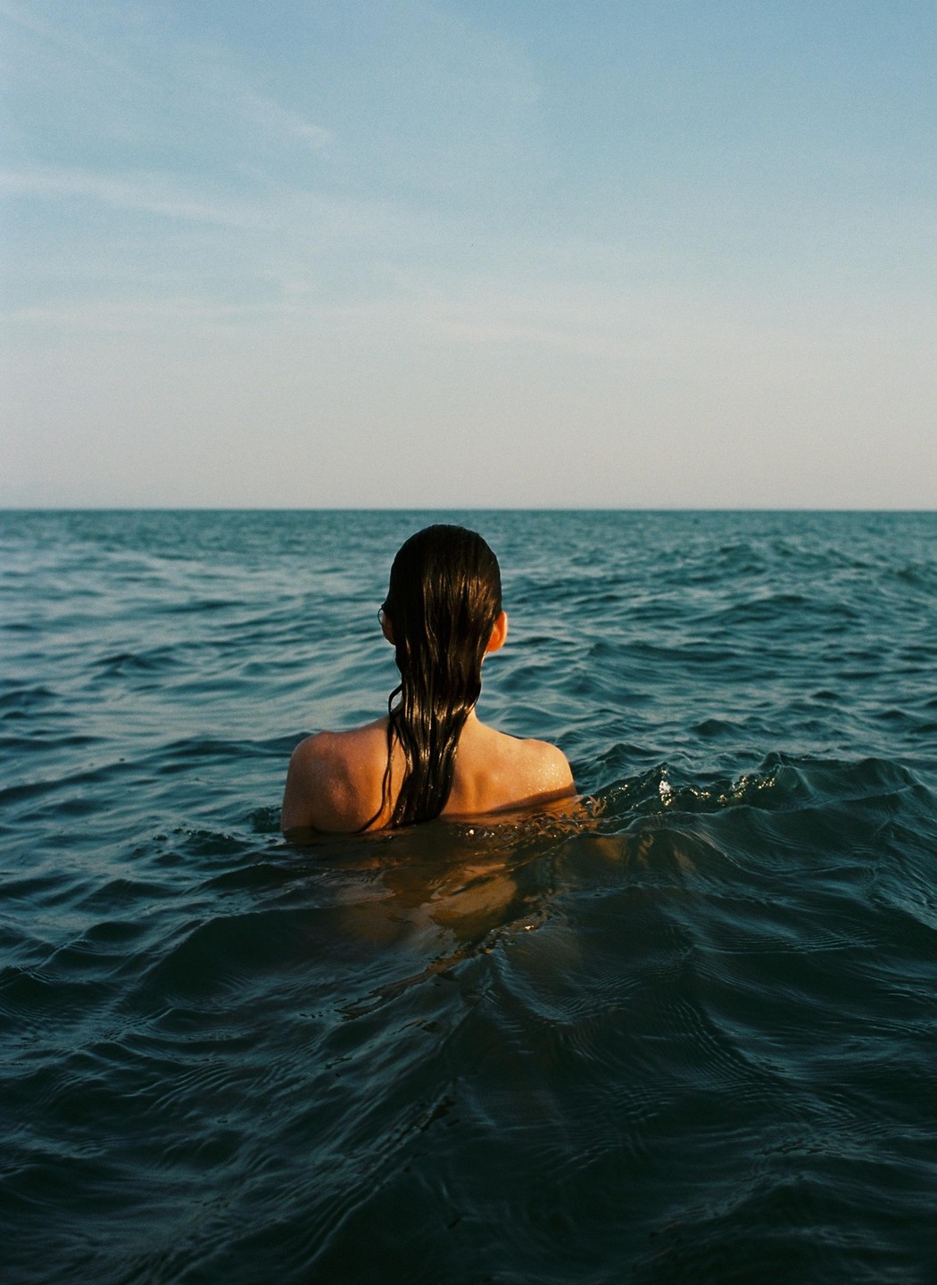 A woman with wet hair is seen from behind, swimming in the ocean.