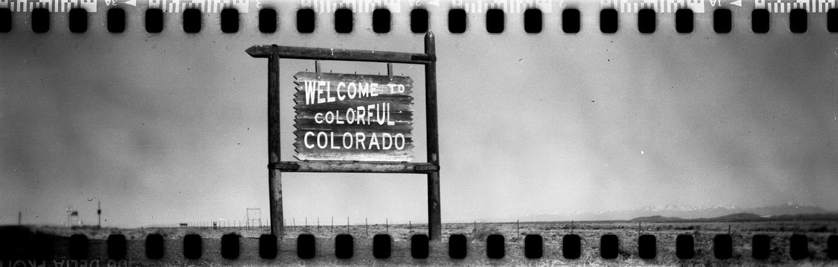 A "Welcome to Colorful Colorado" sign stands in a barren landscape with mountains in the distance.