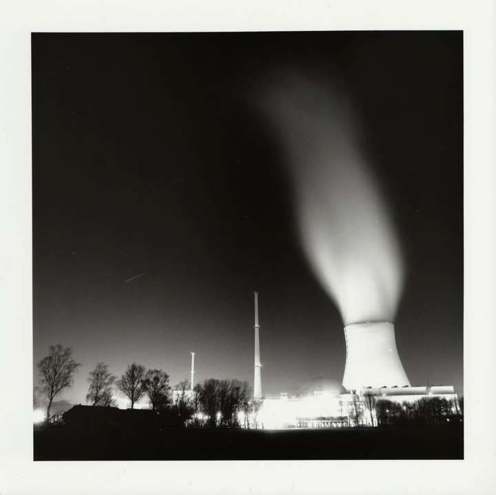 A nuclear power plant with a large cooling tower emitting steam is illuminated at night.