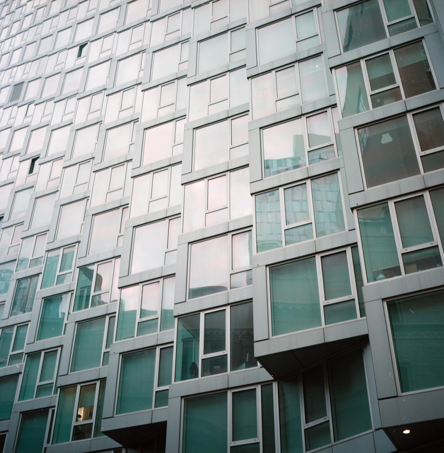 A modern building with many windows reflects the sky and surrounding structures.