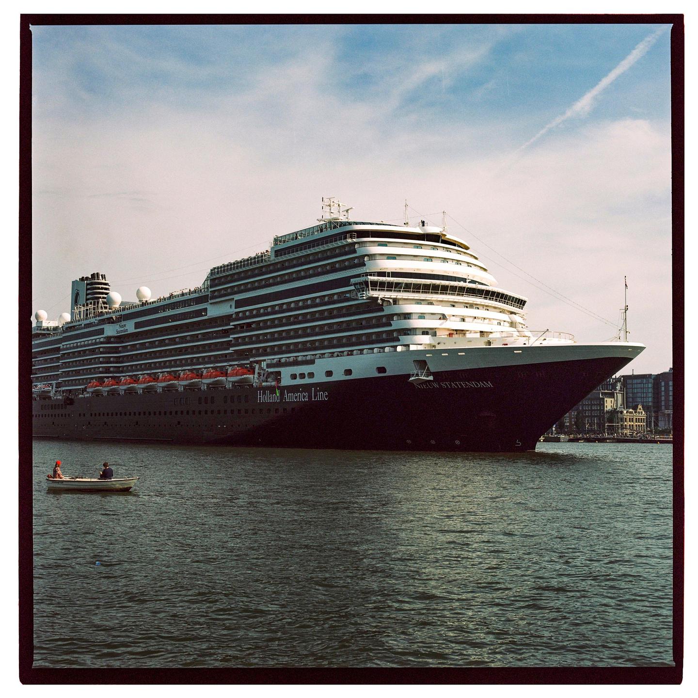 A small boat with two people floats on the water next to a large cruise ship.
