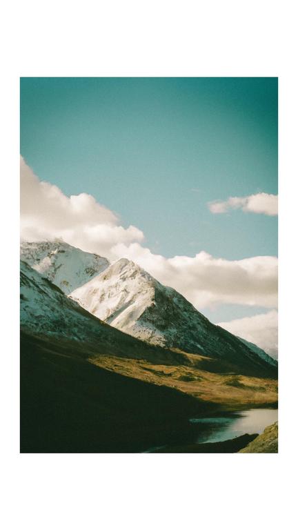 Snow-capped mountains rise above a lake with a clear blue sky and clouds.