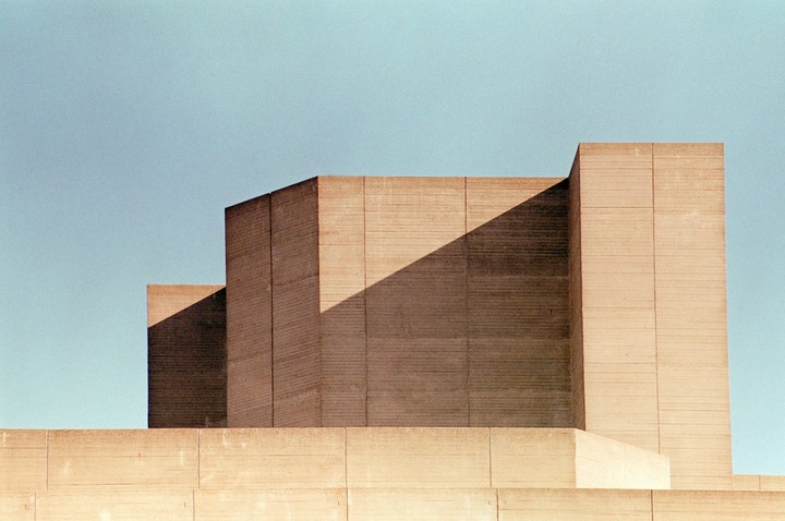 A brutalist concrete building with strong shadows is set against a clear sky.