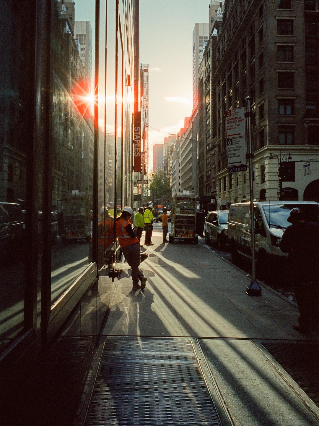 A group of construction workers stand on a city street with long shadows cast by the setting sun.