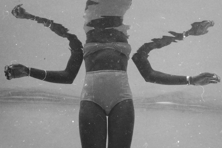 A woman in a two-piece swimsuit is submerged in water with her arms outstretched.